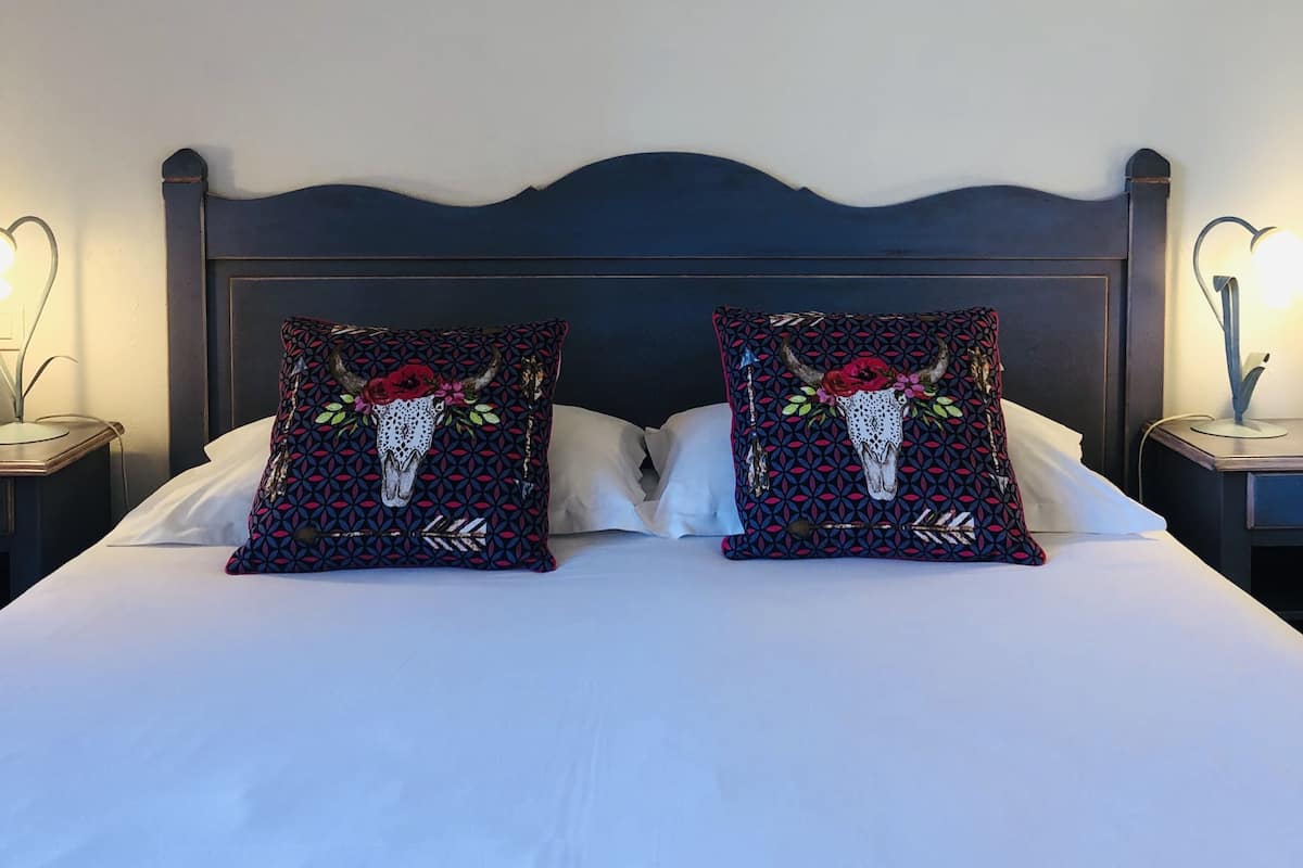 Un lit avec deux coussins décoratifs, une tête de lit sombre et deux tableaux encadrés accrochés au mur.