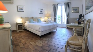 A hotel room with a large bed, two bedside lamps, a small table, a chair, and a window with curtains. - Le Jas Neuf (Sainte-Maxime)