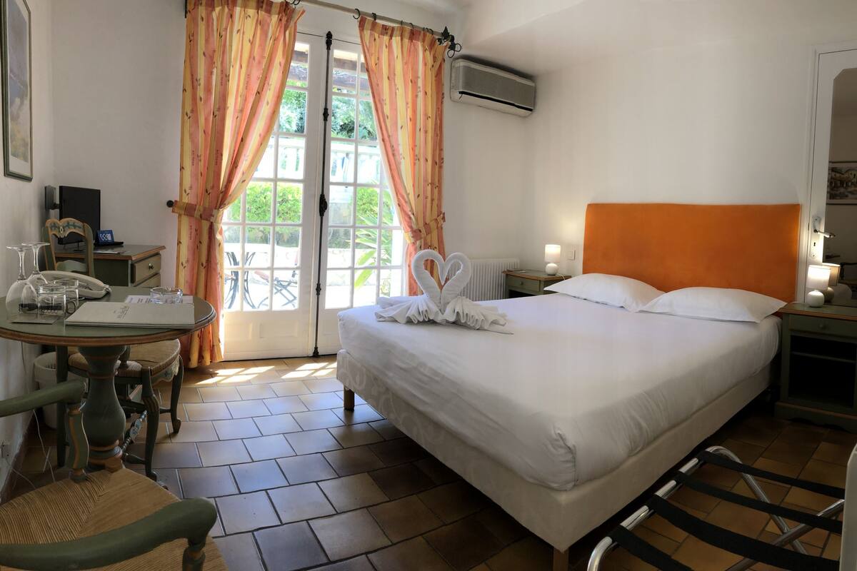 Une chambre d’hôtel avec un lit, un bureau avec un téléphone, une chaise et une table avec des verres et une lampe.