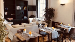 A modern living room with a sofa, a dining table set for two, and a bookshelf. - Le Jas Neuf (Sainte-Maxime)