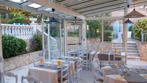 An outdoor patio with tables and chairs, stone walls, and a glass enclosure. - Le Jas Neuf (Sainte-Maxime)