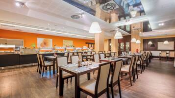 A modern restaurant with a long counter, multiple dining tables, and a kitchen area in the background.