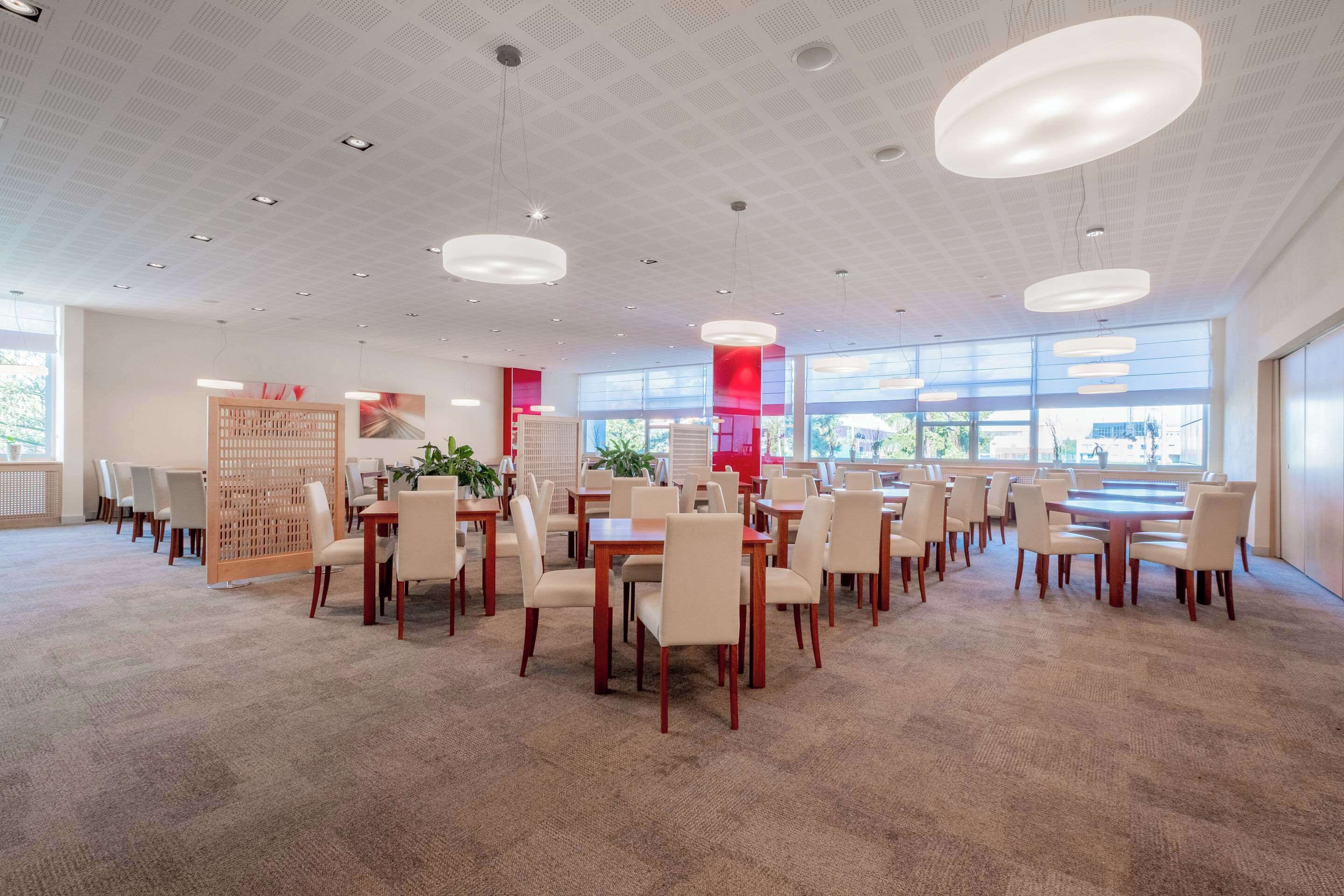 A spacious dining area with multiple tables and chairs, large windows, and modern pendant lighting.