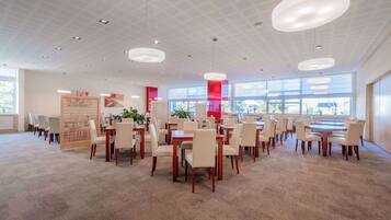 A spacious dining area with multiple tables and chairs, large windows, and modern pendant lighting.