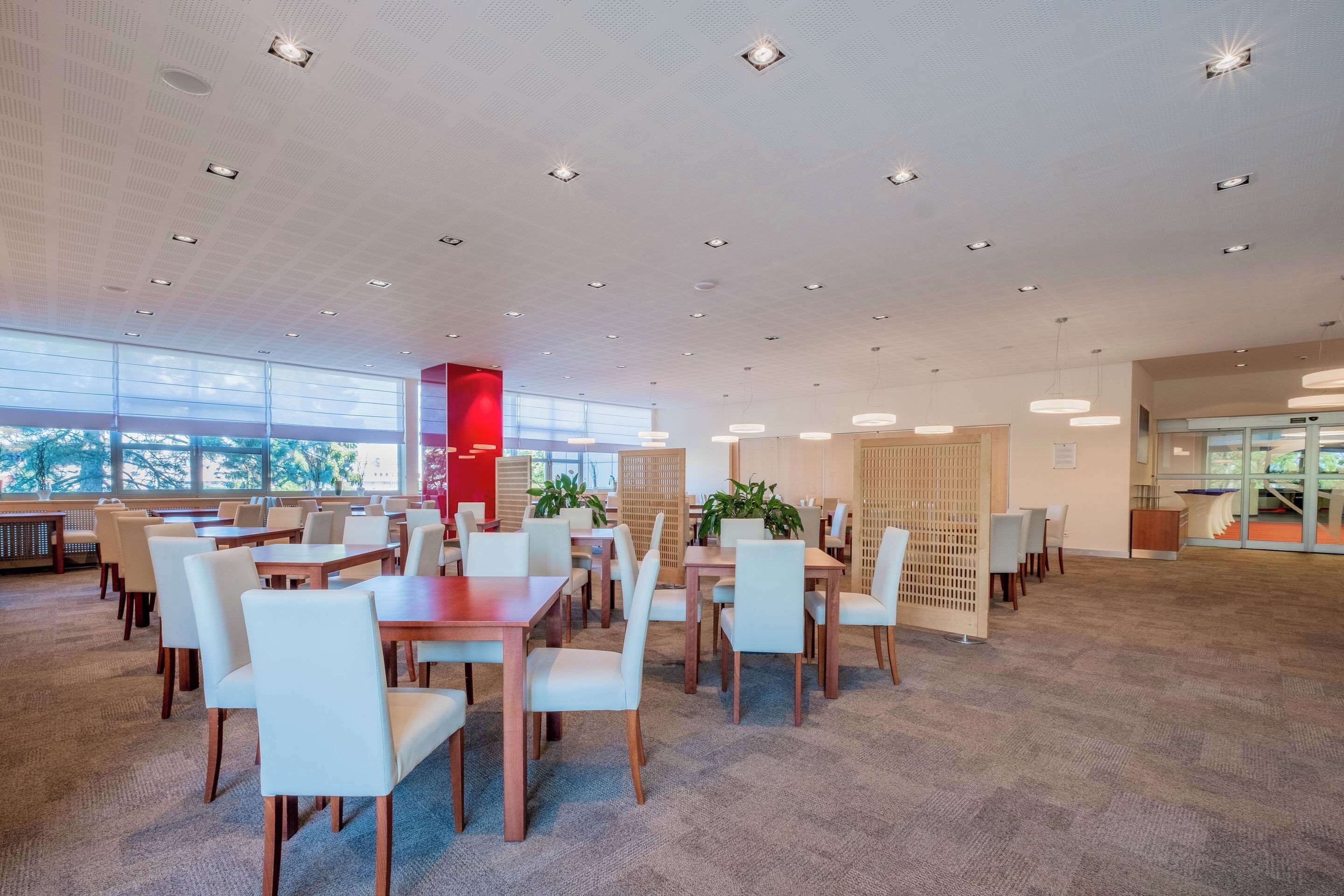 A spacious indoor area with multiple tables and chairs, large windows, and ceiling lights.