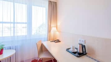 Ein Hotelzimmer mit Schreibtisch, Stuhl, Lampe, Telefon, Kaffeemaschine und einem kleinen Tisch mit Topfpflanze.