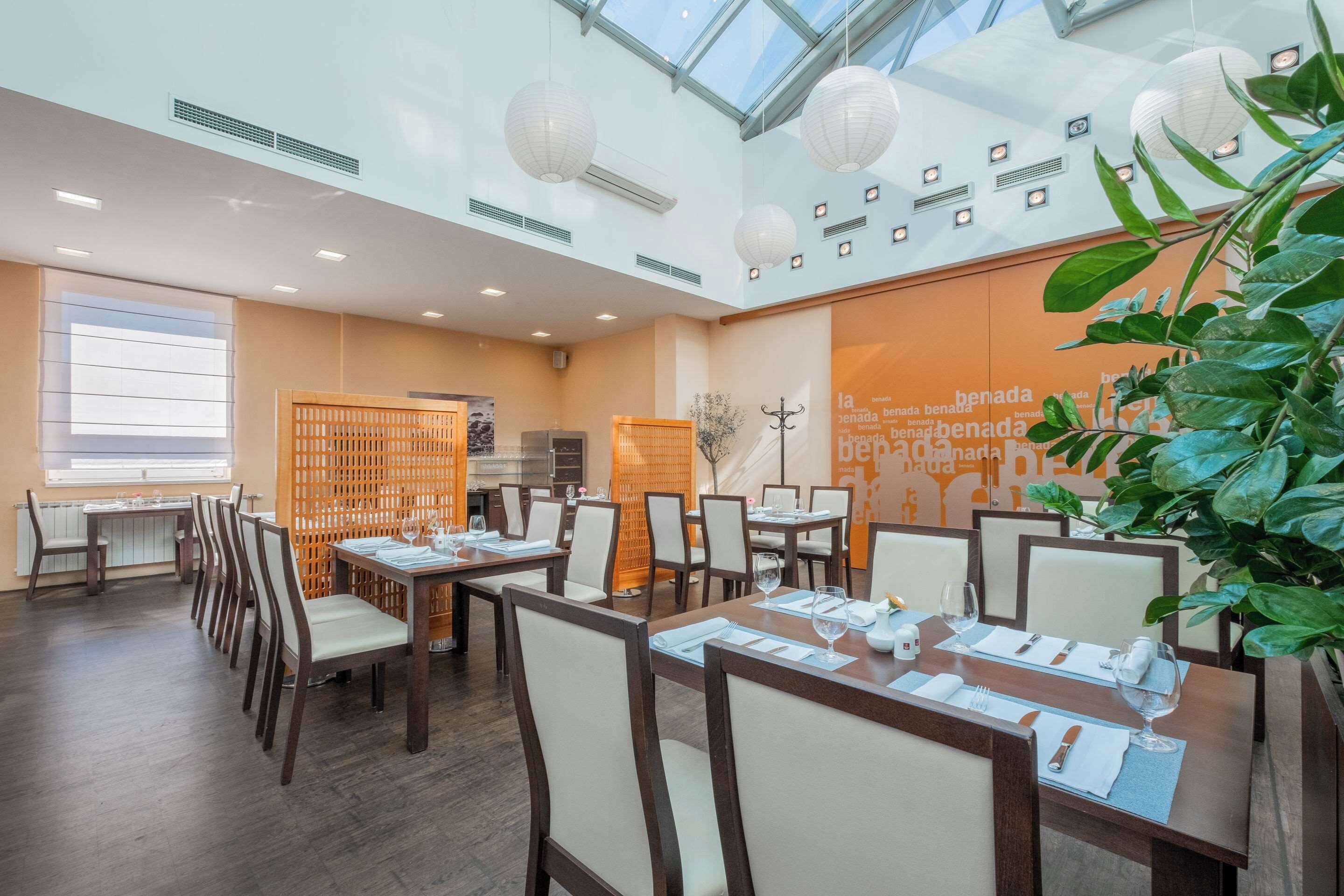 A modern dining area with tables set for guests, a large window, and a decorative plant.