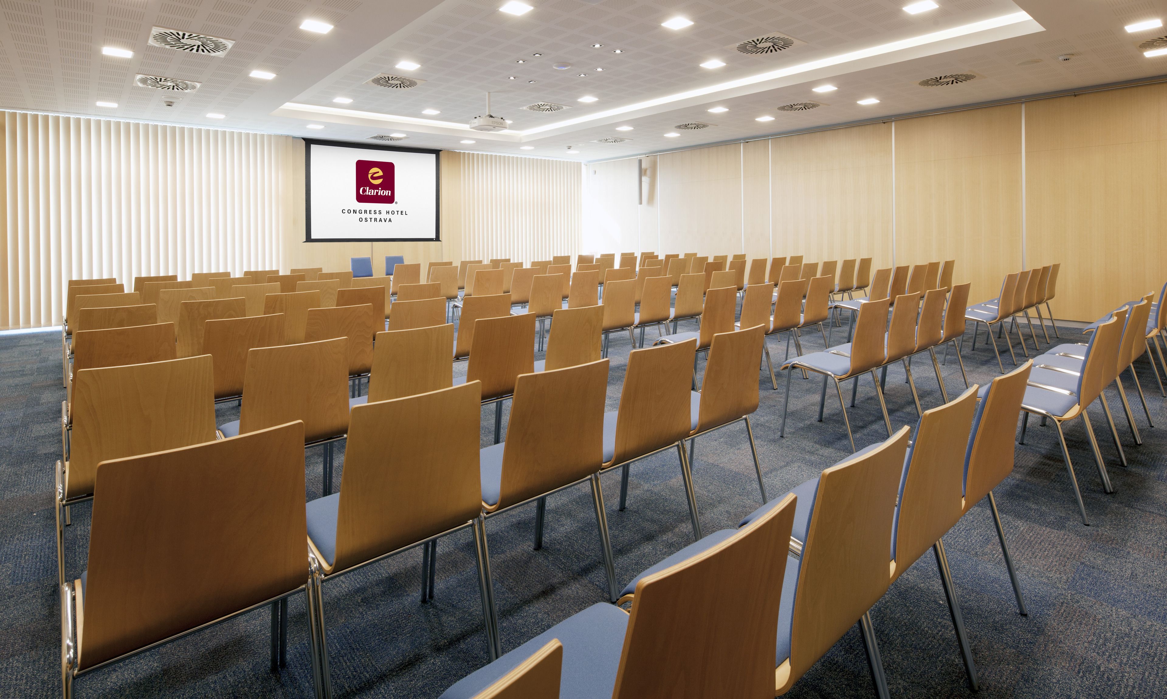 A conference room with rows of chairs, a projector screen, and a ceiling with recessed lighting.