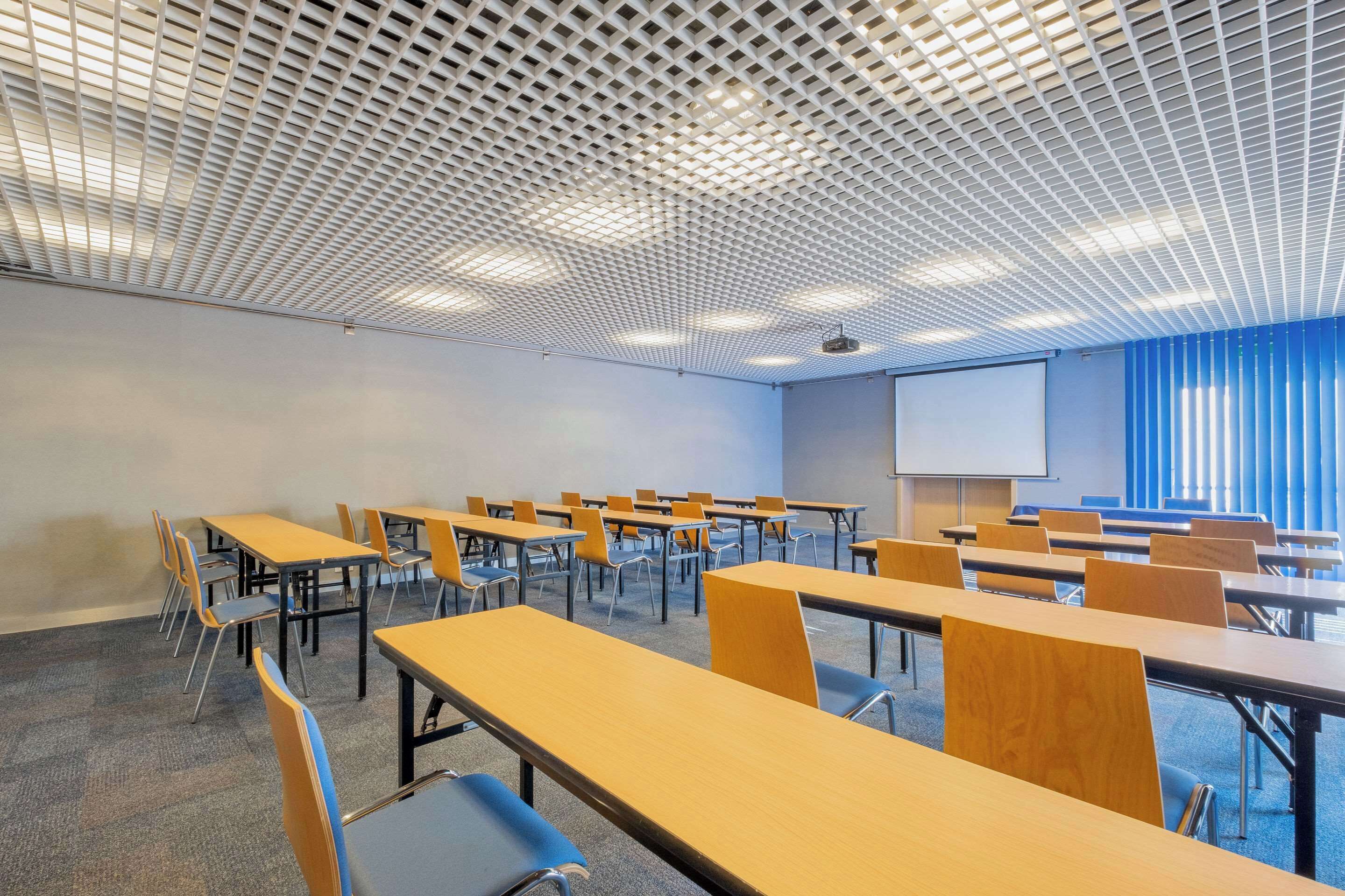 A classroom with rows of desks and chairs, a projector screen, and a presentation screen.