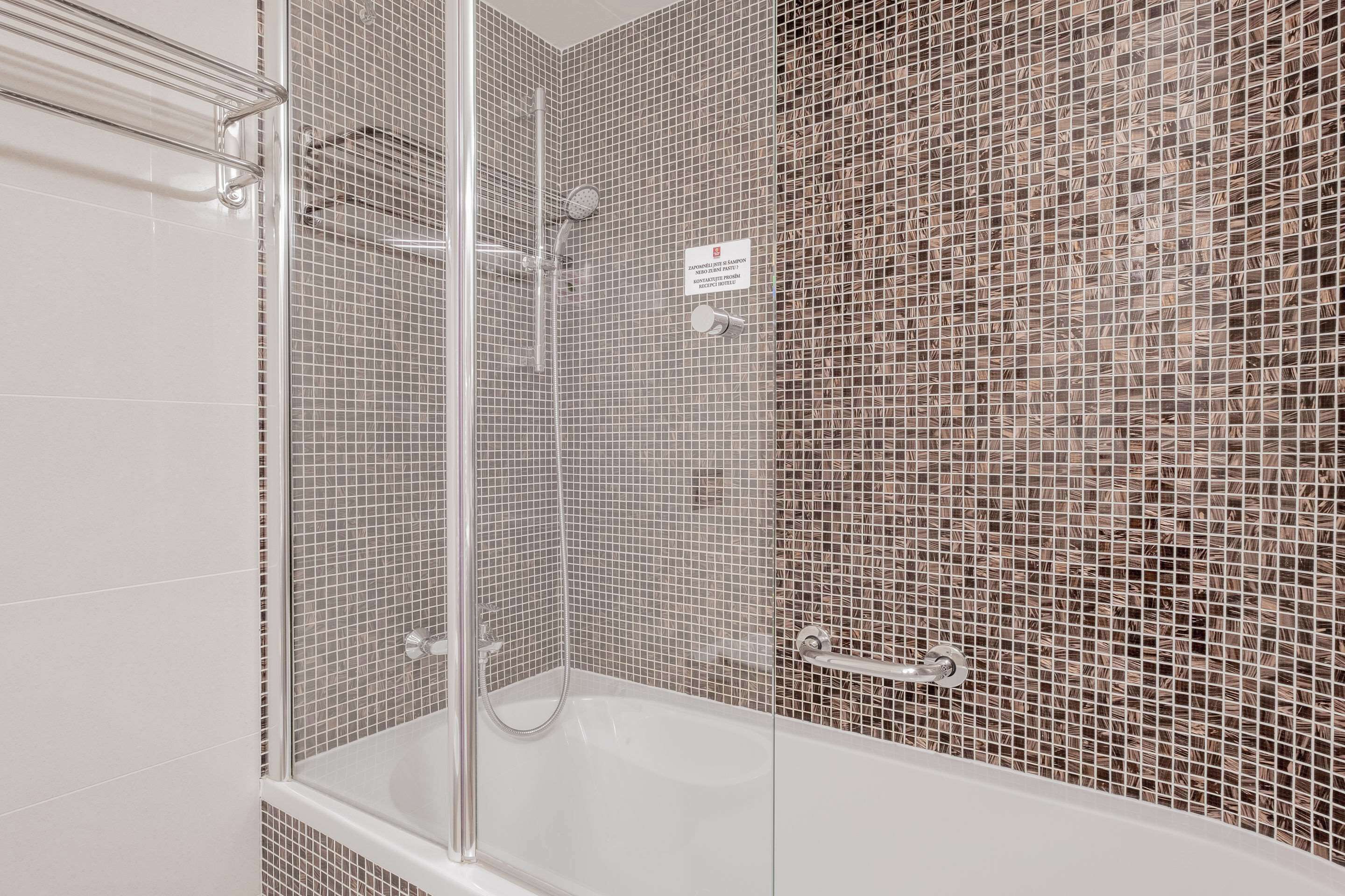 A modern bathroom with a glass-enclosed shower, a white bathtub, and mosaic tile walls.