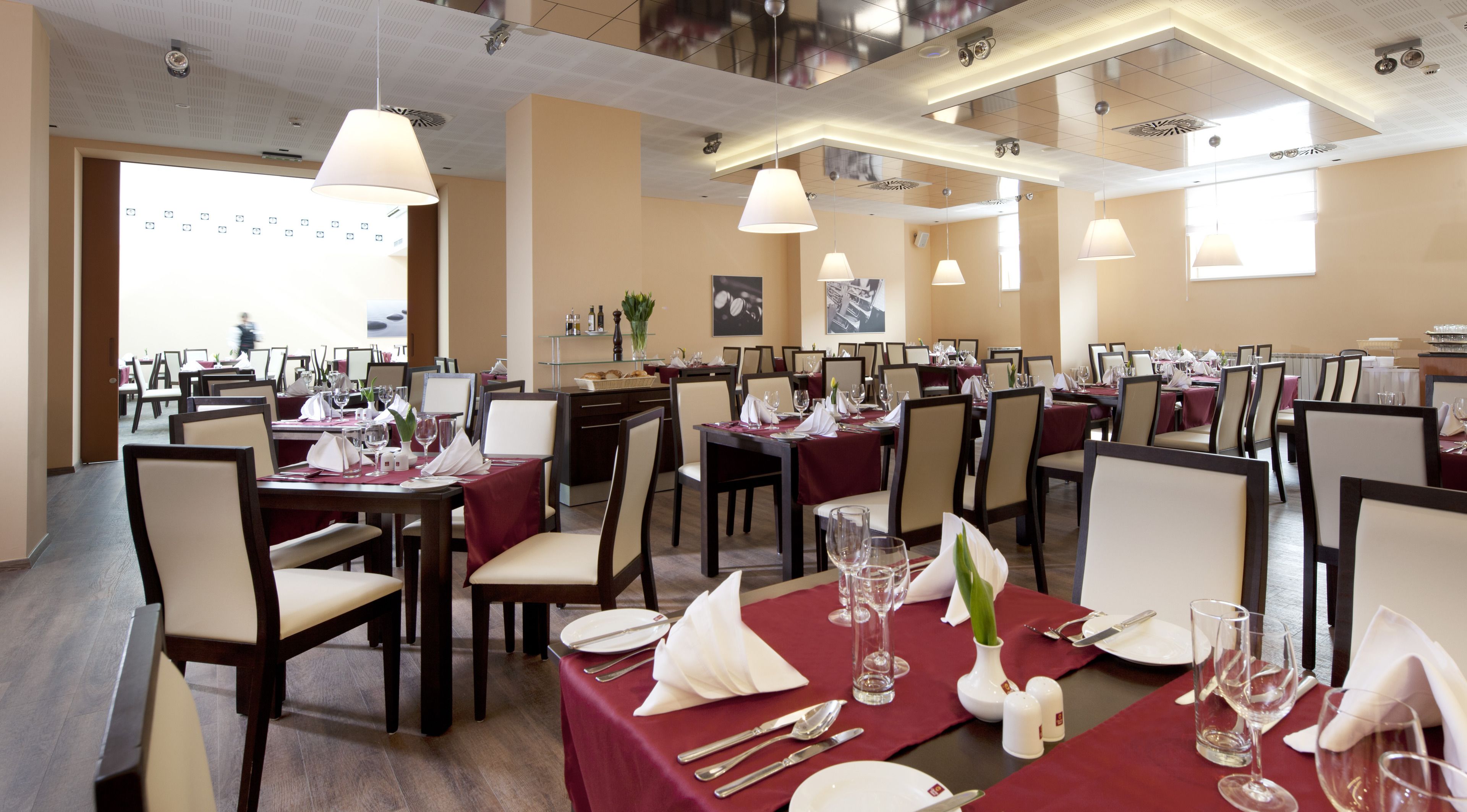 A restaurant with multiple dining tables set for guests, featuring a modern interior with pendant lighting and a neutral color palette.