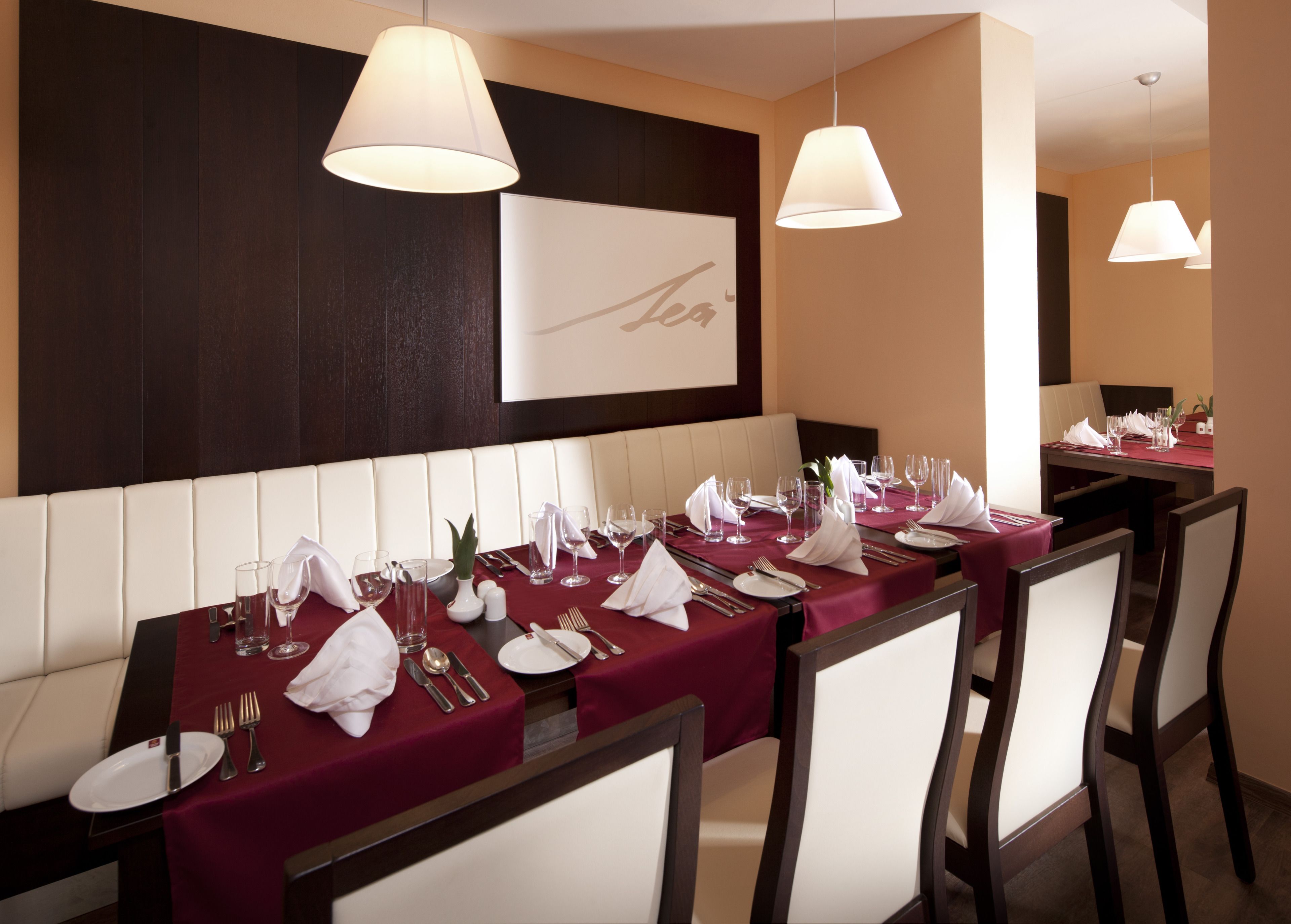 A restaurant with a long table set for dining, featuring white chairs and a red tablecloth.