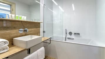 A modern bathroom with a white sink, a glass shower enclosure, and a wooden vanity.