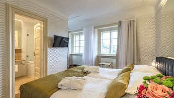 A hotel room with a bed, a TV, a window with curtains, and a bathroom visible through an open door.