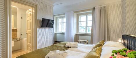 A hotel room with a bed, a TV, a window with curtains, and a bathroom visible through an open door.