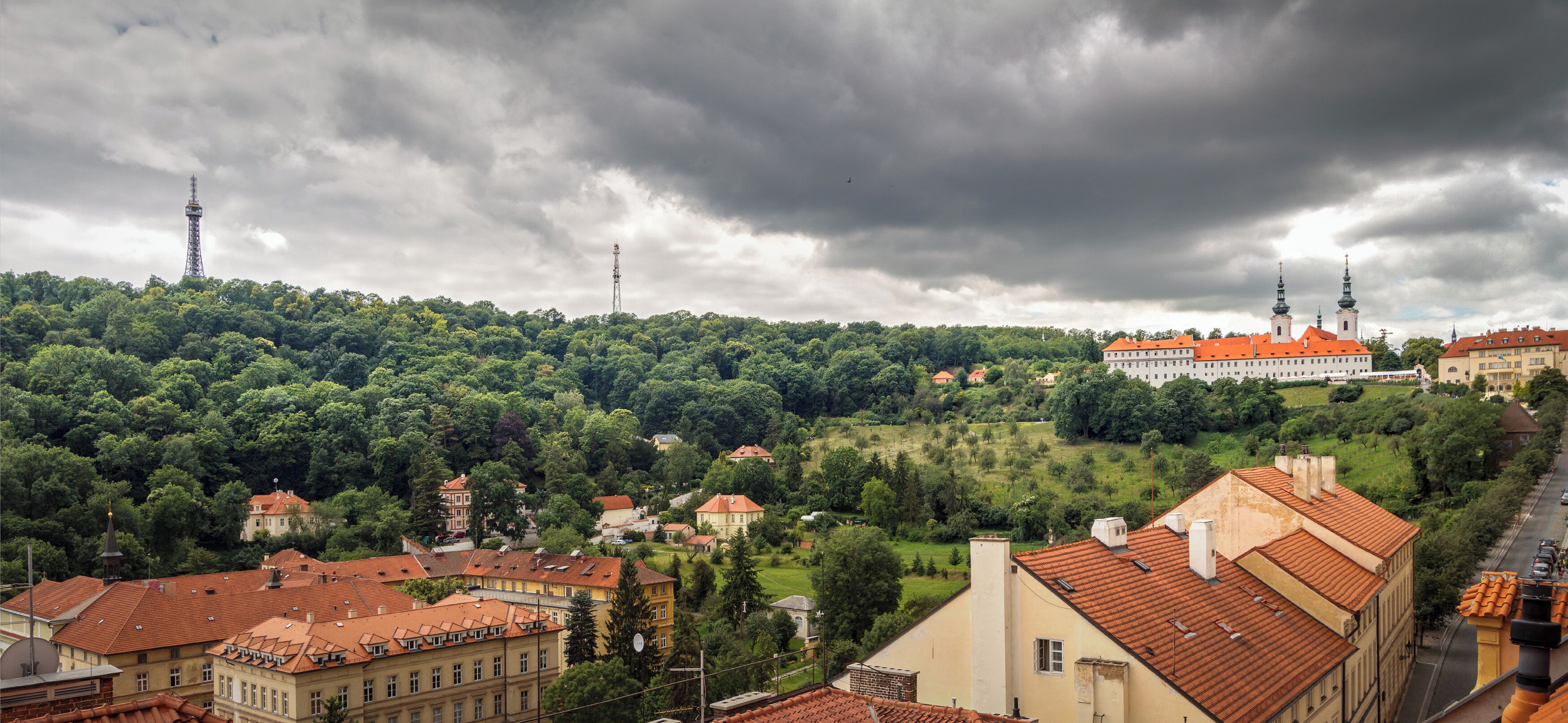 A cityscape with a prominent building with a red roof, surrounded by lush greenery and other buildings with similar architecture.