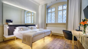 Quarto de hotel moderno com cama, mesa de cabeceira, televisão e janela com cortinas.