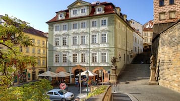 Un bâtiment historique à la façade classique, doté d’un escalier menant à un étage supérieur et d’un espace extérieur aménagé avec des parasols.