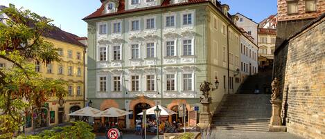 A historic building with a classical facade, a staircase leading to an upper level, and outdoor seating with umbrellas.