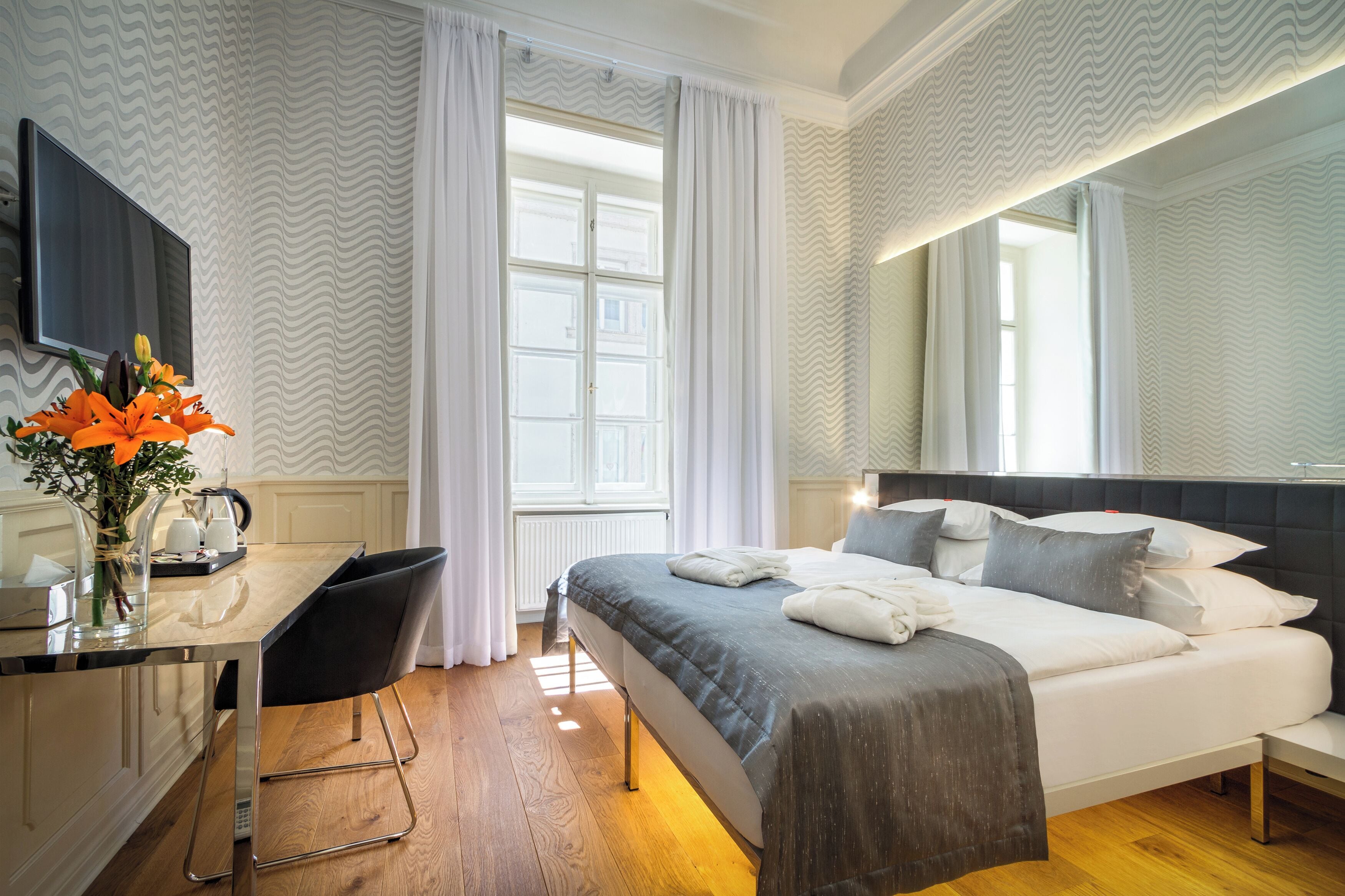 A hotel room with a bed, a desk, a chair, a TV, and a window with curtains.