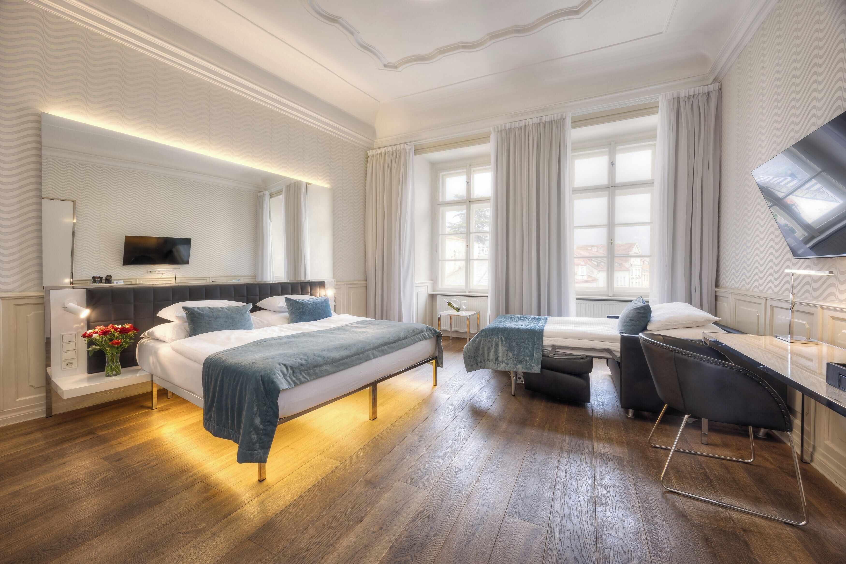 A modern hotel room with a large bed, a desk, a chair, and a television.
