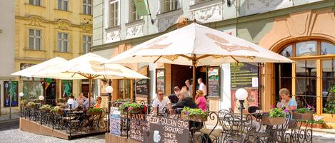 Un café al aire libre con mesas y sombrillas, rodeado de edificios históricos.