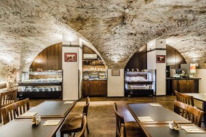Restaurante com teto de pedra rústica, mesas de madeira e um espaço para buffet.
