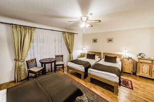 Quarto de hotel com duas camas, uma escrivaninha, uma cadeira, um ventilador de teto e uma mesa de cabeceira com abajur.