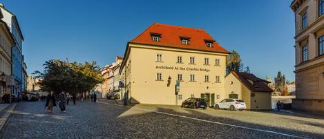 Una calle empedrada con edificios históricos, uno con un letrero que dice 'Archibald At The Charles Bridge'.