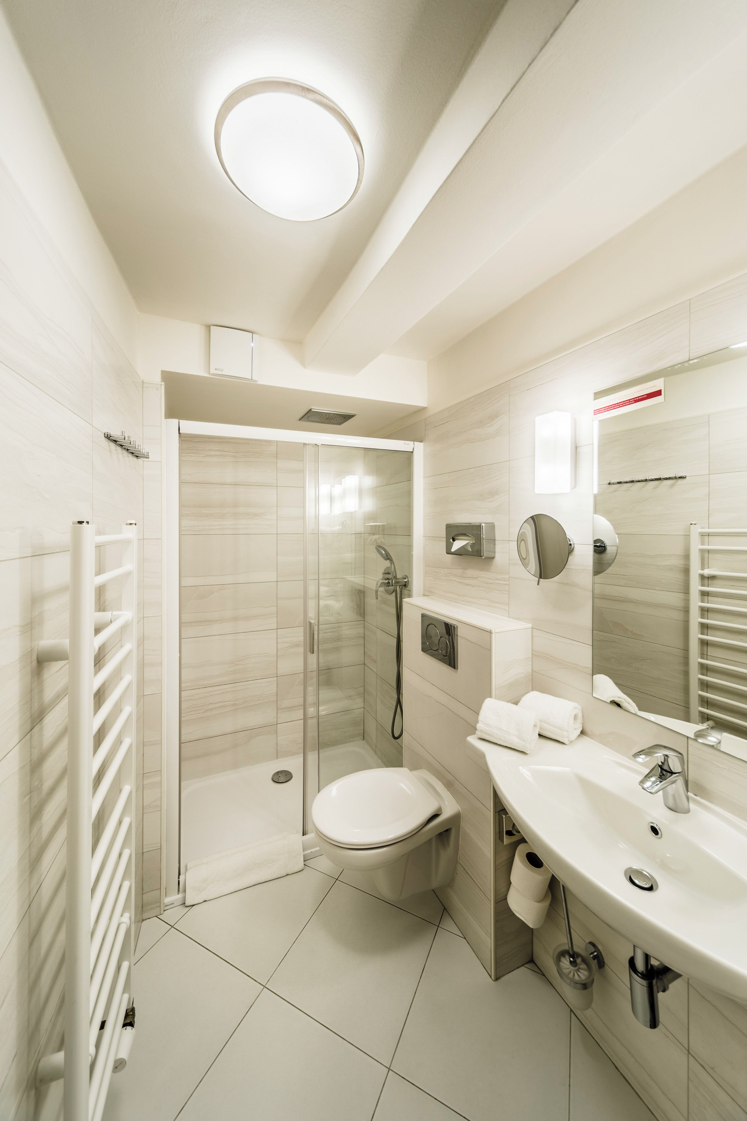 Et moderne badeværelse med bruseniche i glas, toilet, vask med spejl og et håndklædeholder.