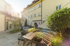 A courtyard with a wooden table and benches, surrounded by buildings with multiple windows and a small tree. - Archibald At the Charles Bridge (Prague)