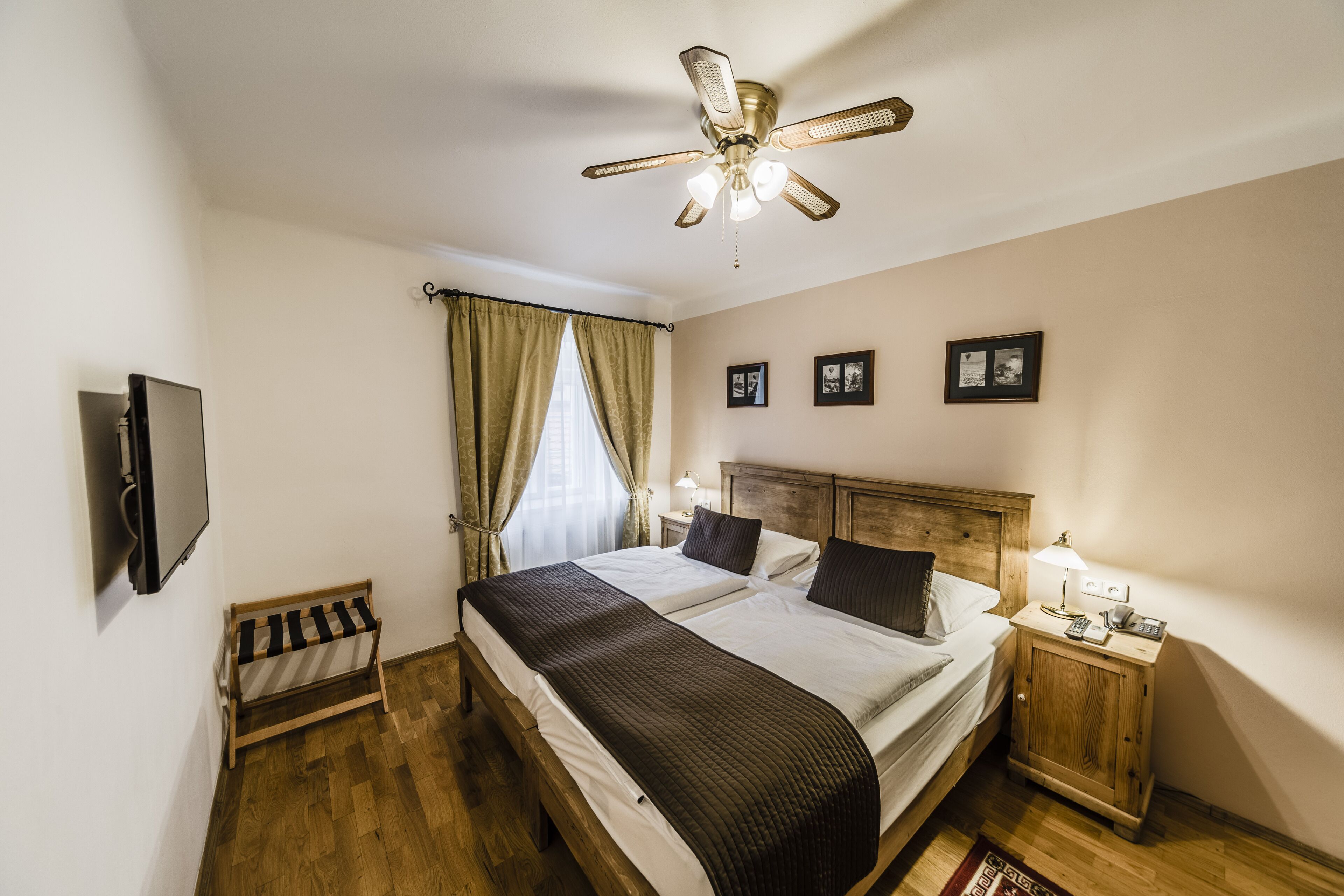 A bedroom with a bed, a nightstand, a TV, a ceiling fan, and a window with curtains.