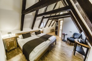 Quarto com uma cama grande, vigas de madeira, uma mesa pequena e uma cadeira.