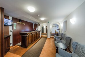 Aula, jossa on puinen vastaanottotiski, seinäkello ja oleskelualue, jossa on kuviollisia tuoleja.