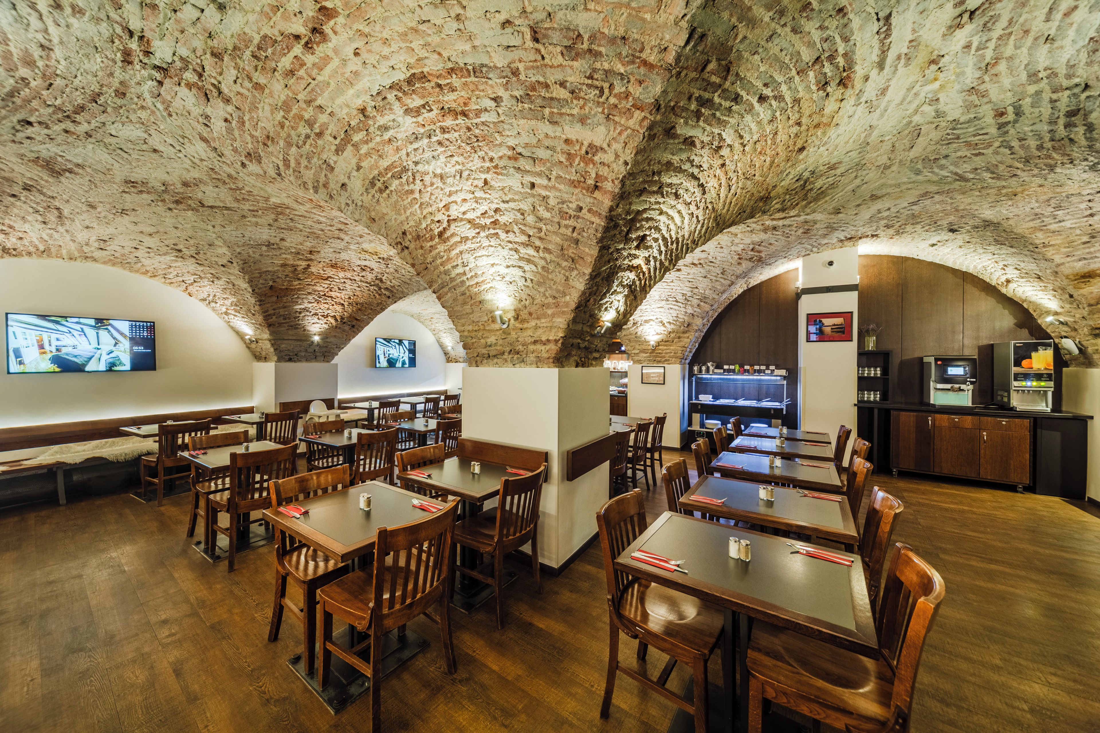 Un interior con techos de ladrillo en arco, mesas y sillas de madera, y una zona de bar con una pantalla de televisión.