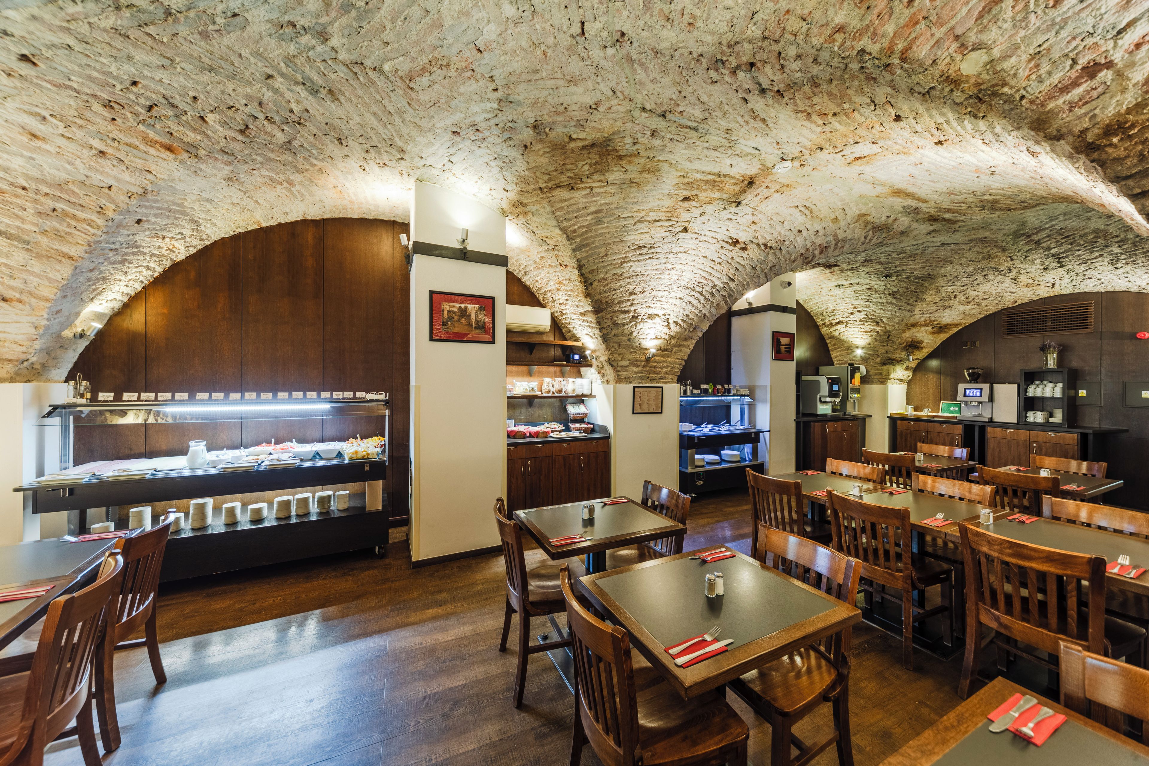 A restaurant with a rustic stone ceiling, wooden tables and chairs, and a buffet area with various food items.