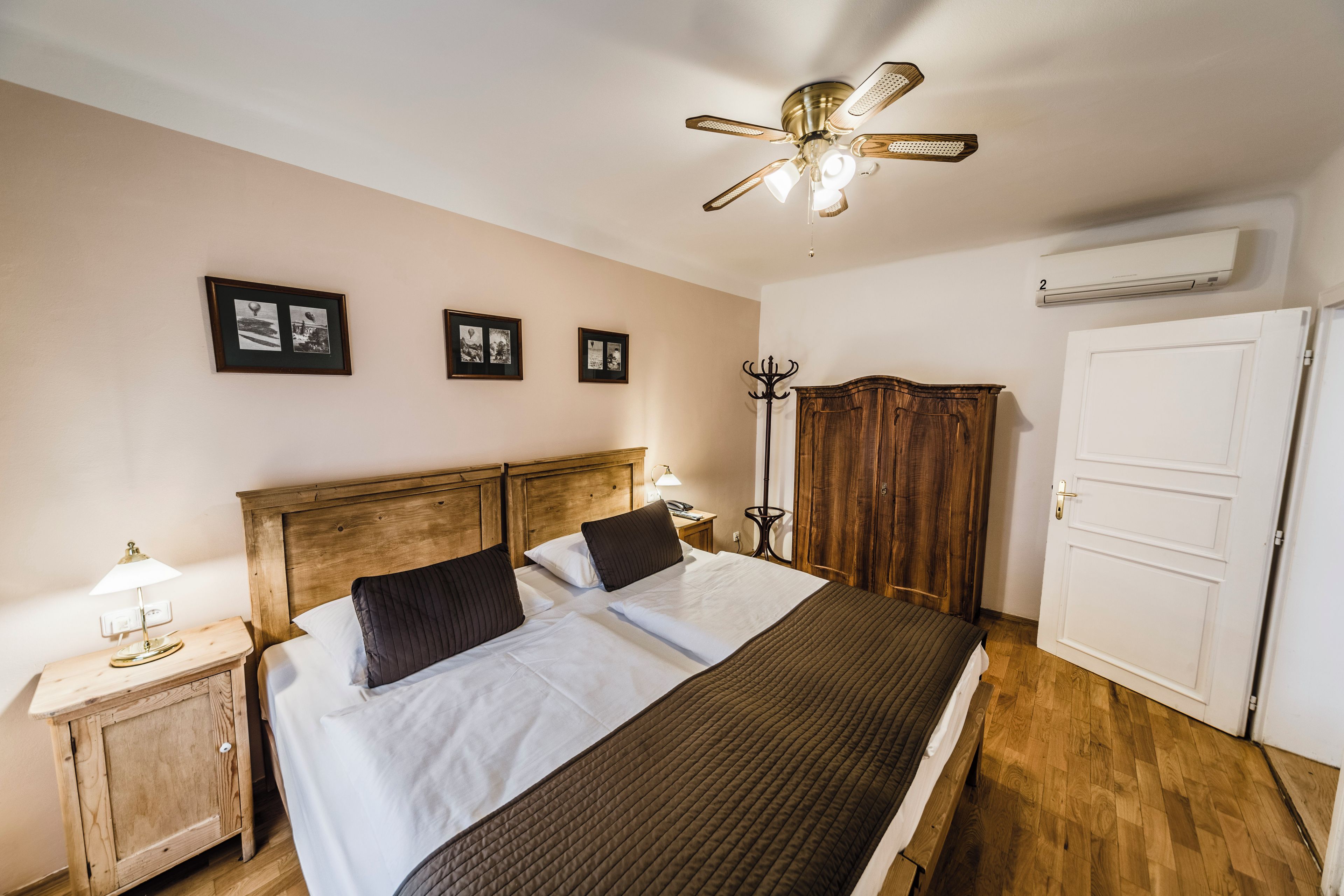 Een slaapkamer met een houten hoofdbord, een bed met witte lakens, een plafondventilator en een kledingkast.