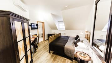 A bedroom with a bed, bedside table, lamp, and a TV on the wall.