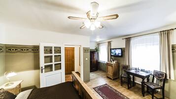 A hotel room with a bed, a desk with chairs, a television, and a ceiling fan.