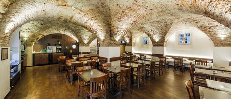Ein Restaurant mit rustikalem Stein-Gewölbe, Holztischen und -stühlen.