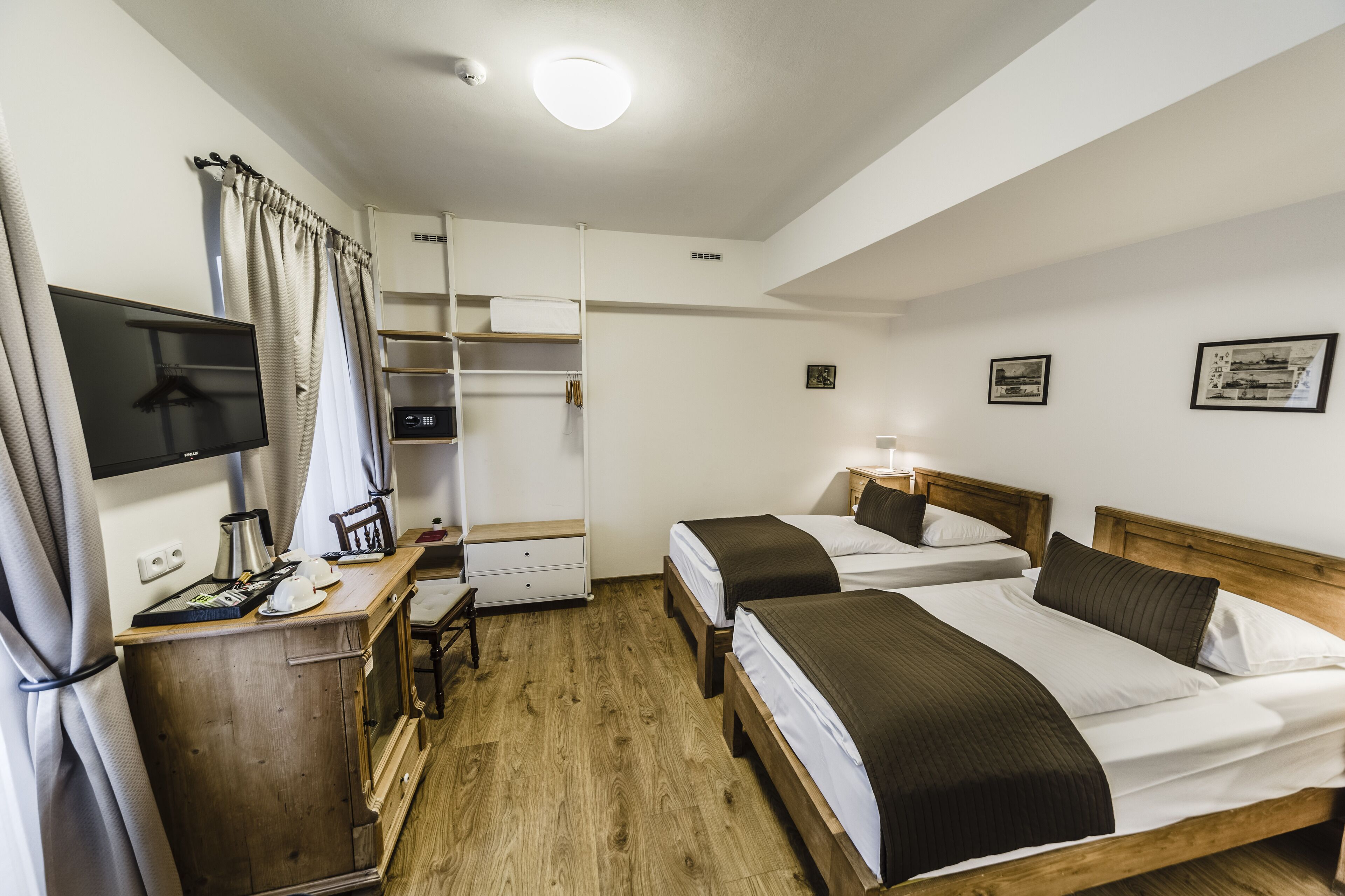 A hotel room with two beds, a desk with a computer, a wardrobe, and a television.