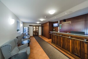 A reception area with a reception desk, a seating area with houndstooth patterned sofas, a vending machine, and a television screen. - Archibald At the Charles Bridge (Prague)