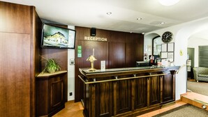 A reception desk with a wooden finish, a television mounted above it, and a clock on the wall. - Archibald At the Charles Bridge (Prague)