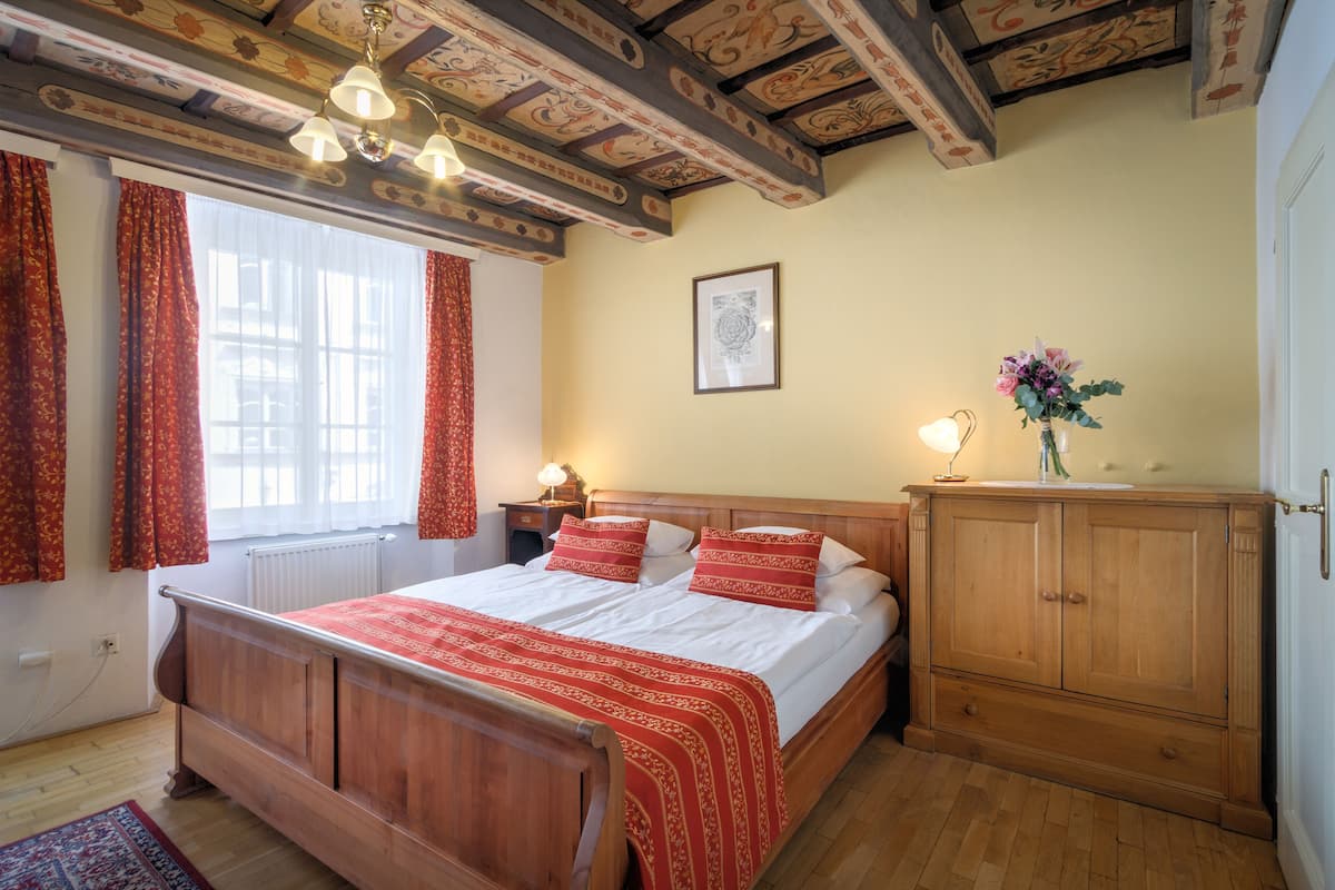 Ein Schlafzimmer mit einem hölzernen Bett, roter Bettwäsche, einem Holzschrank, einer Heizung und einem Fenster mit Vorhängen.