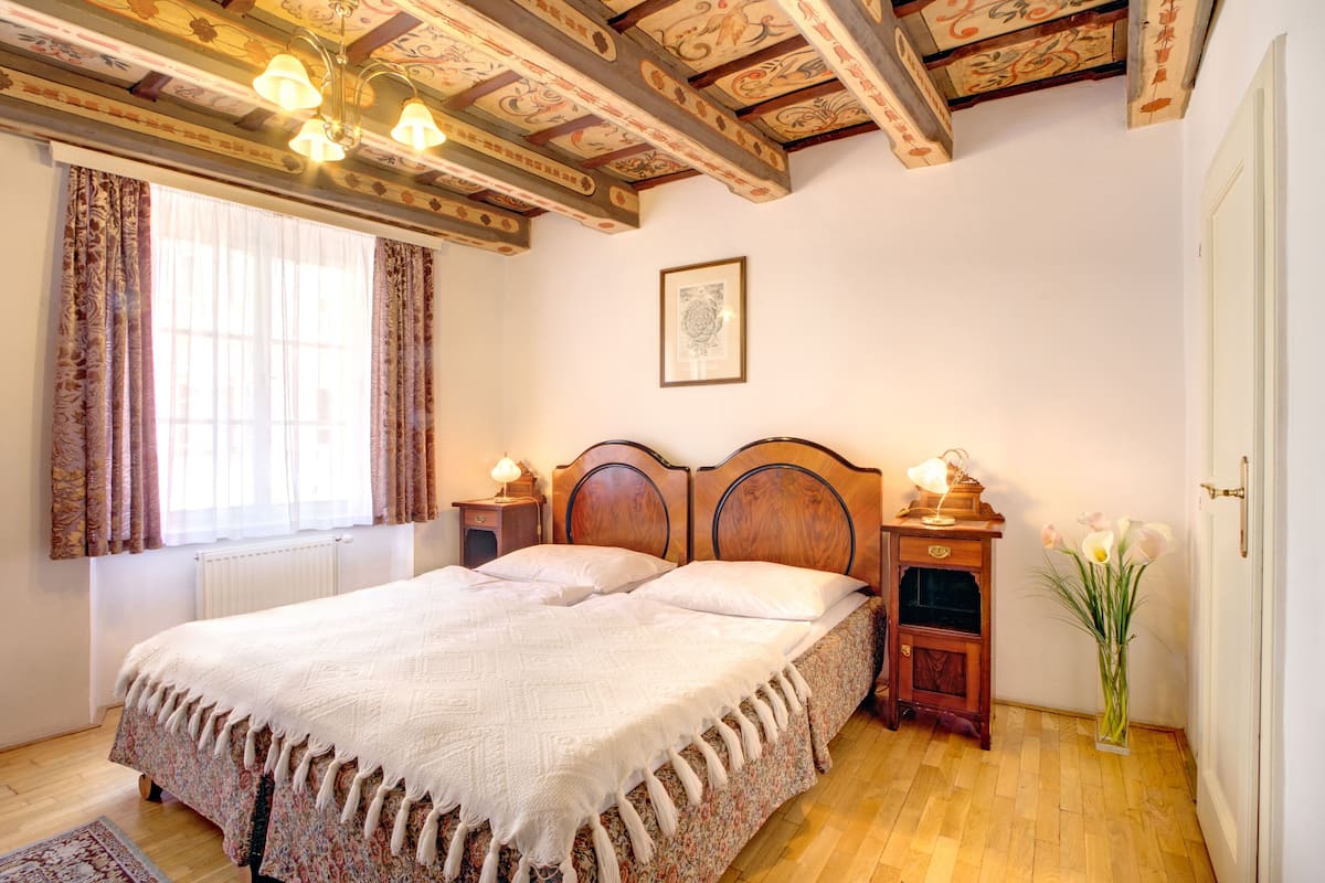 Ein Schlafzimmer mit einem großen Bett, einem hölzernen Kopfteil, Nachttischen mit Lampen, einem gerahmten Bild an der Wand und einer Vase mit Blumen.