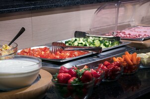 Buffet com diversos alimentos, incluindo pepino fatiado, tomates, cenouras e morangos.
