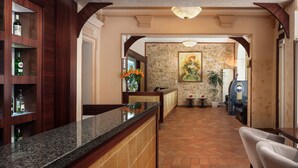A reception area with a reception desk, wooden shelving with bottles, a stone wall with a painting, and a seating area with a couch and chairs. - Hotel Praga 1 (Prague)