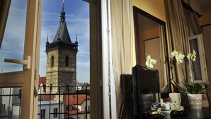 A room with a view of a tower through a window, a desk with a computer, a cup, and a potted orchid. - Hotel Praga 1 (Prague)