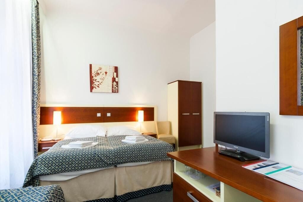 A hotel room with a bed, bedside table, lamp, TV, and a cabinet.