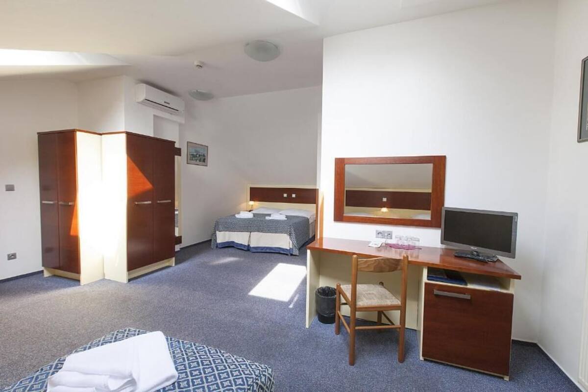 Habitación de hotel con cama, escritorio con computadora, silla, armario y espejo.